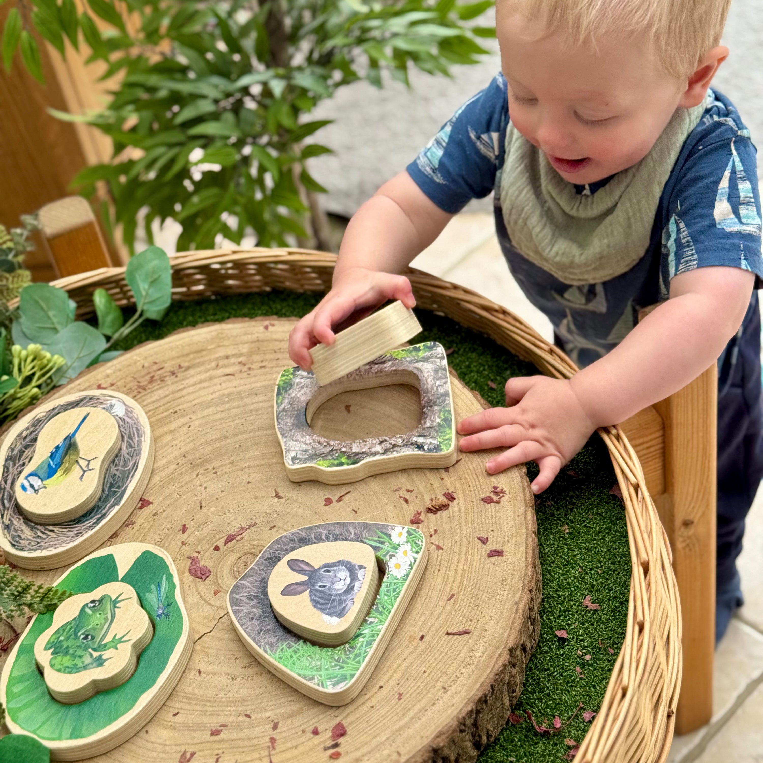 Child playing with wooden nature-themed toys on a round wooden table outdoors.