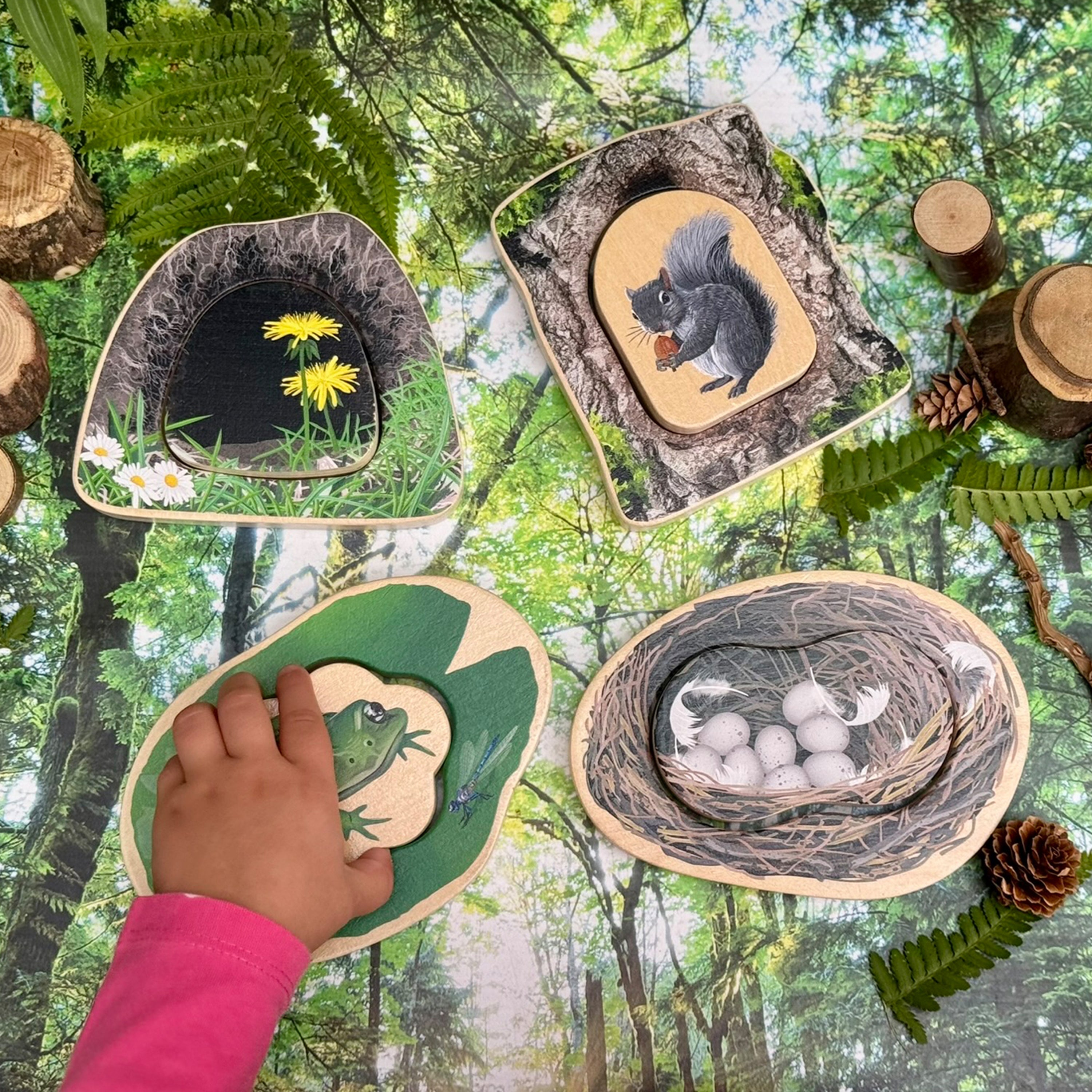 Child's hand interacting with a wooden puzzle of a forest scene, surrounded by natural elements.
