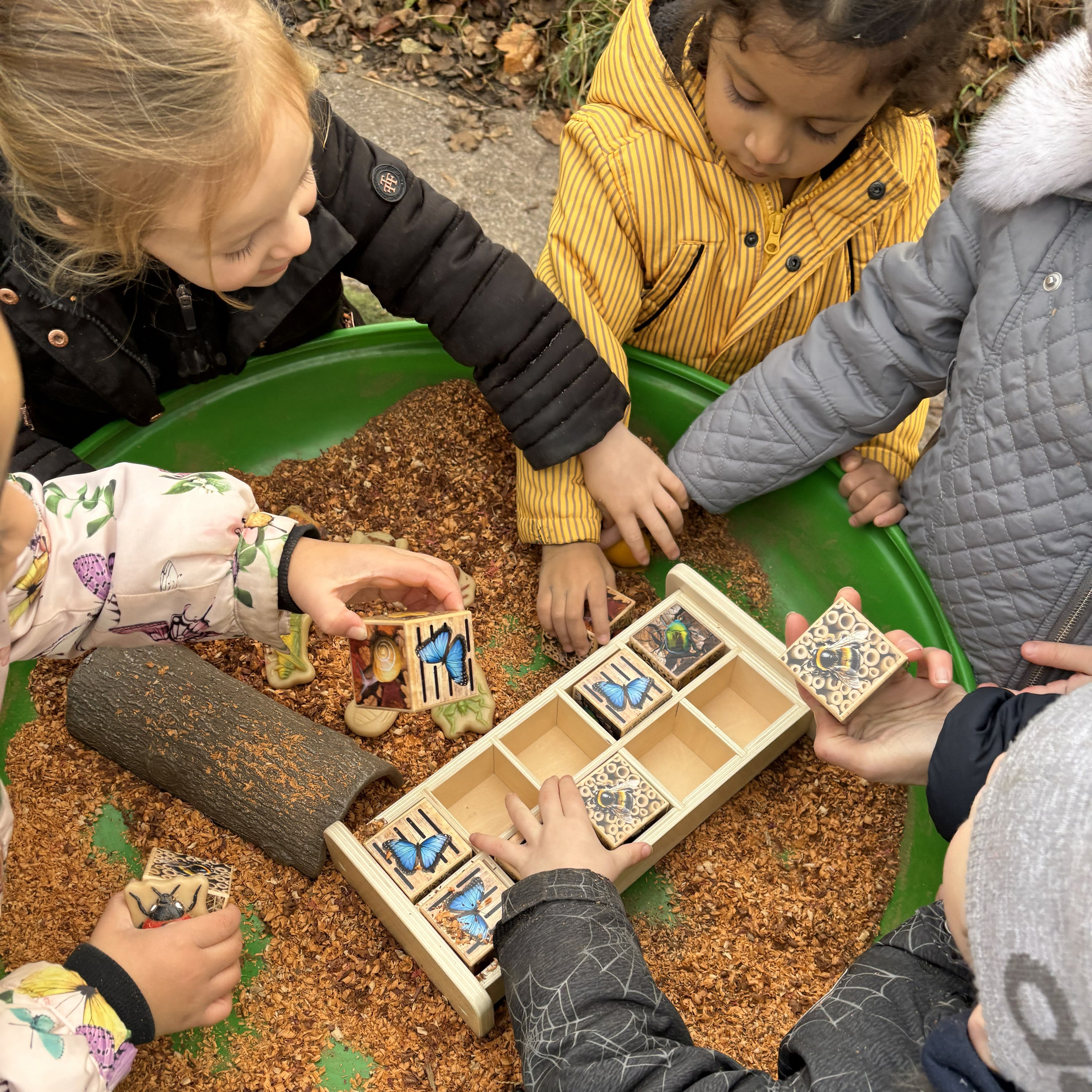 Children playing with wooden nature-themed blocks outdoors.