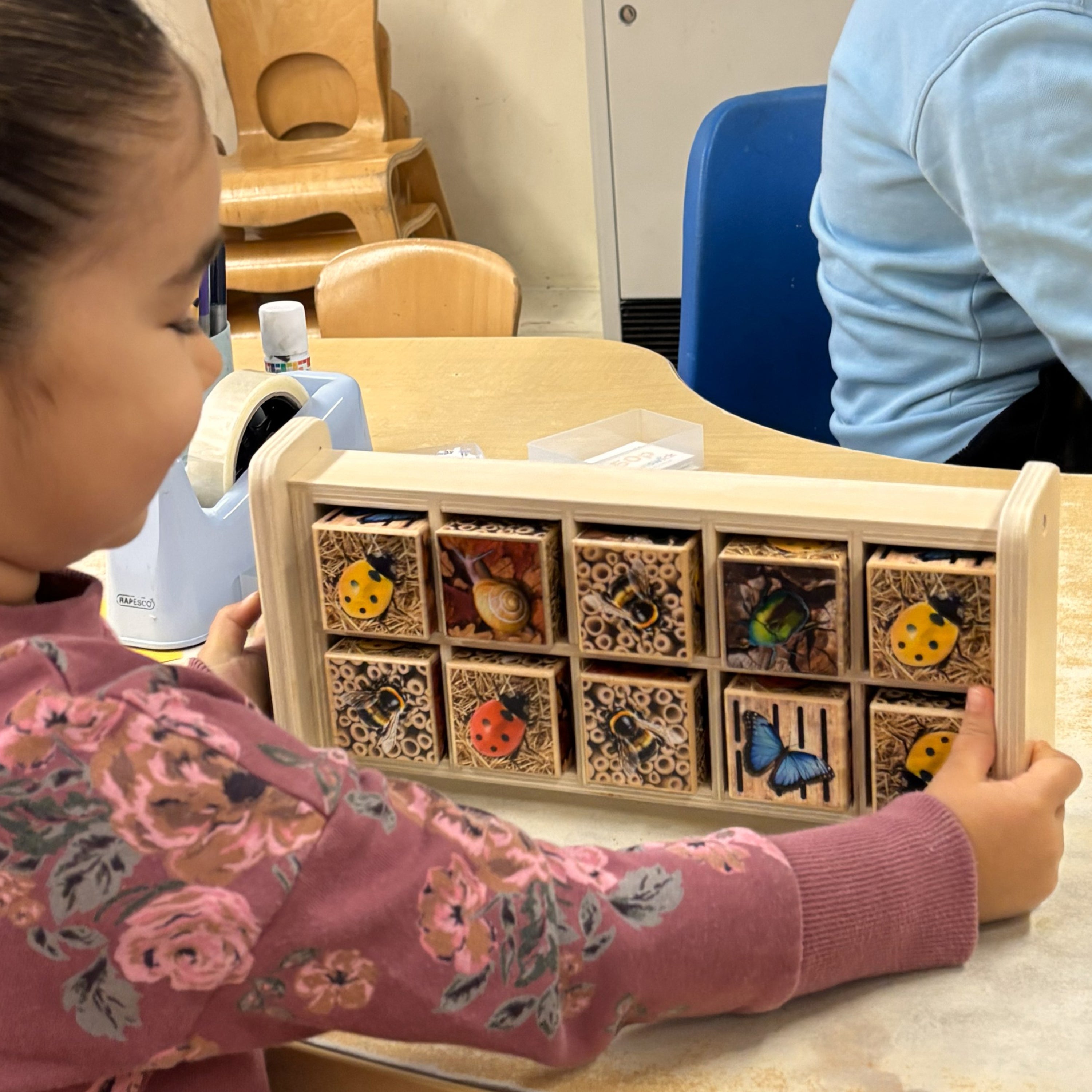 Child playing with a wooden toy box containing animal figurines in a classroom setting.