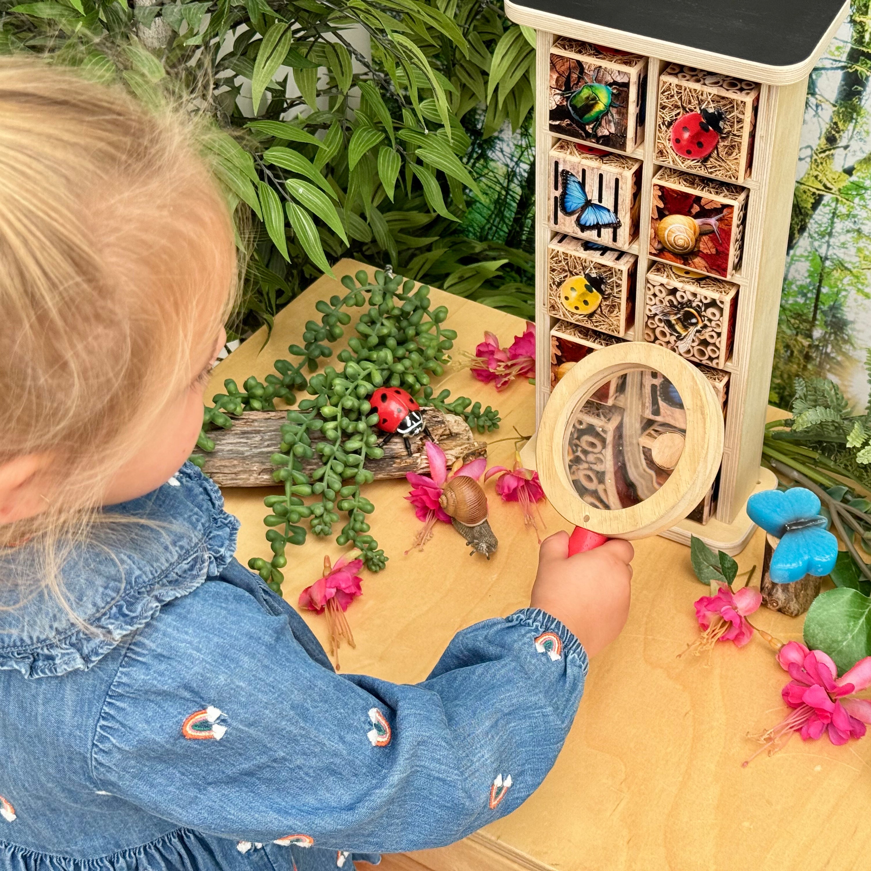 Child playing with a magnifying glass and nature-themed toys on a wooden surface.