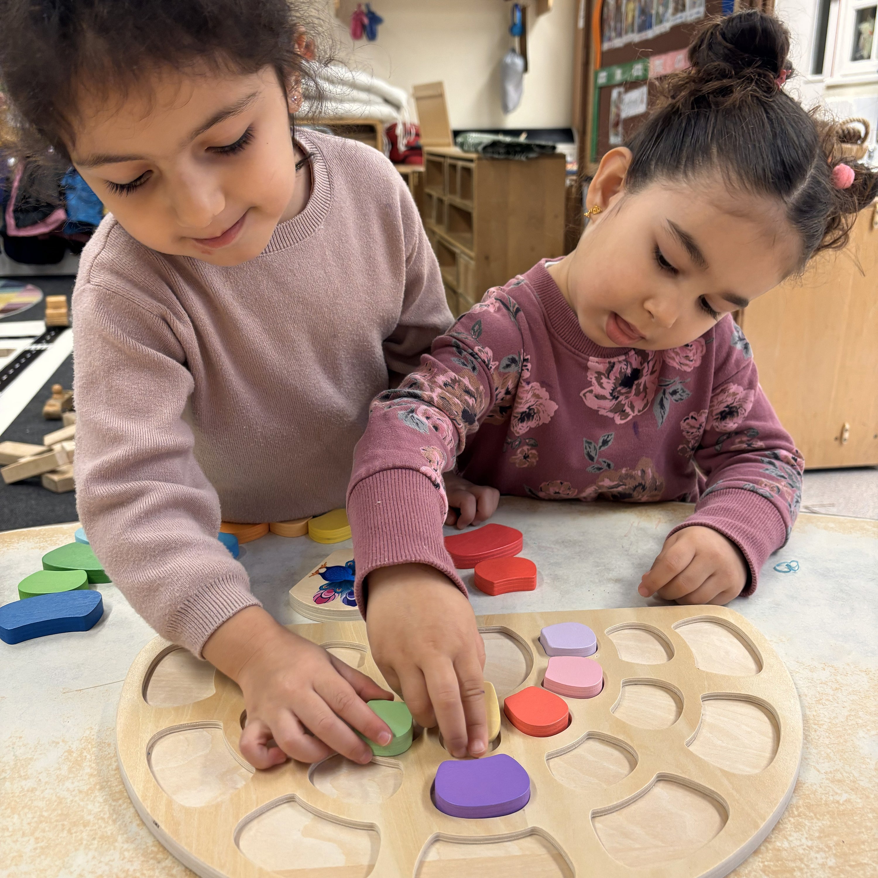 Two young children playing with a wooden puzzle in a classroom setting.