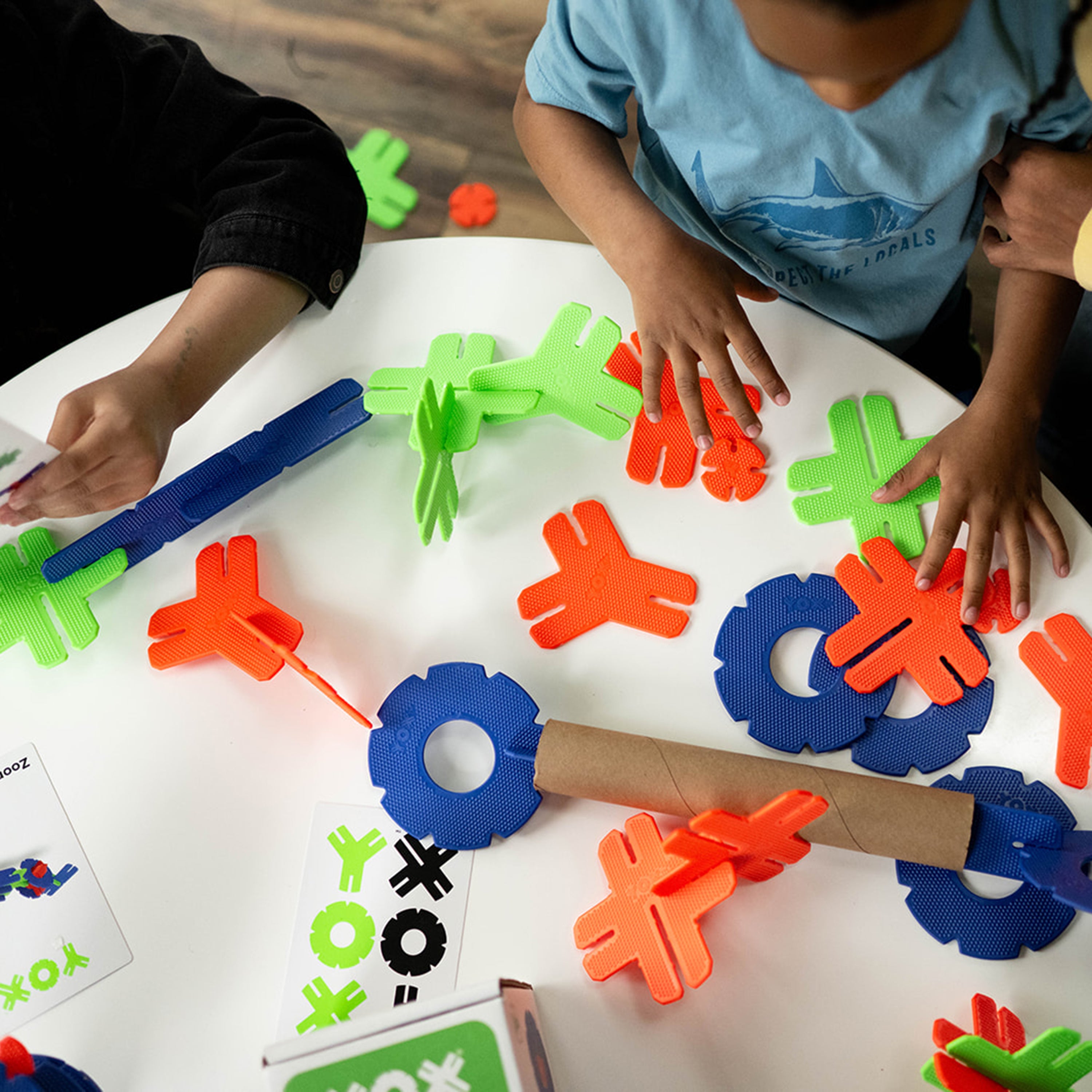 Children playing with colorful plastic letters and shapes on a white surface.