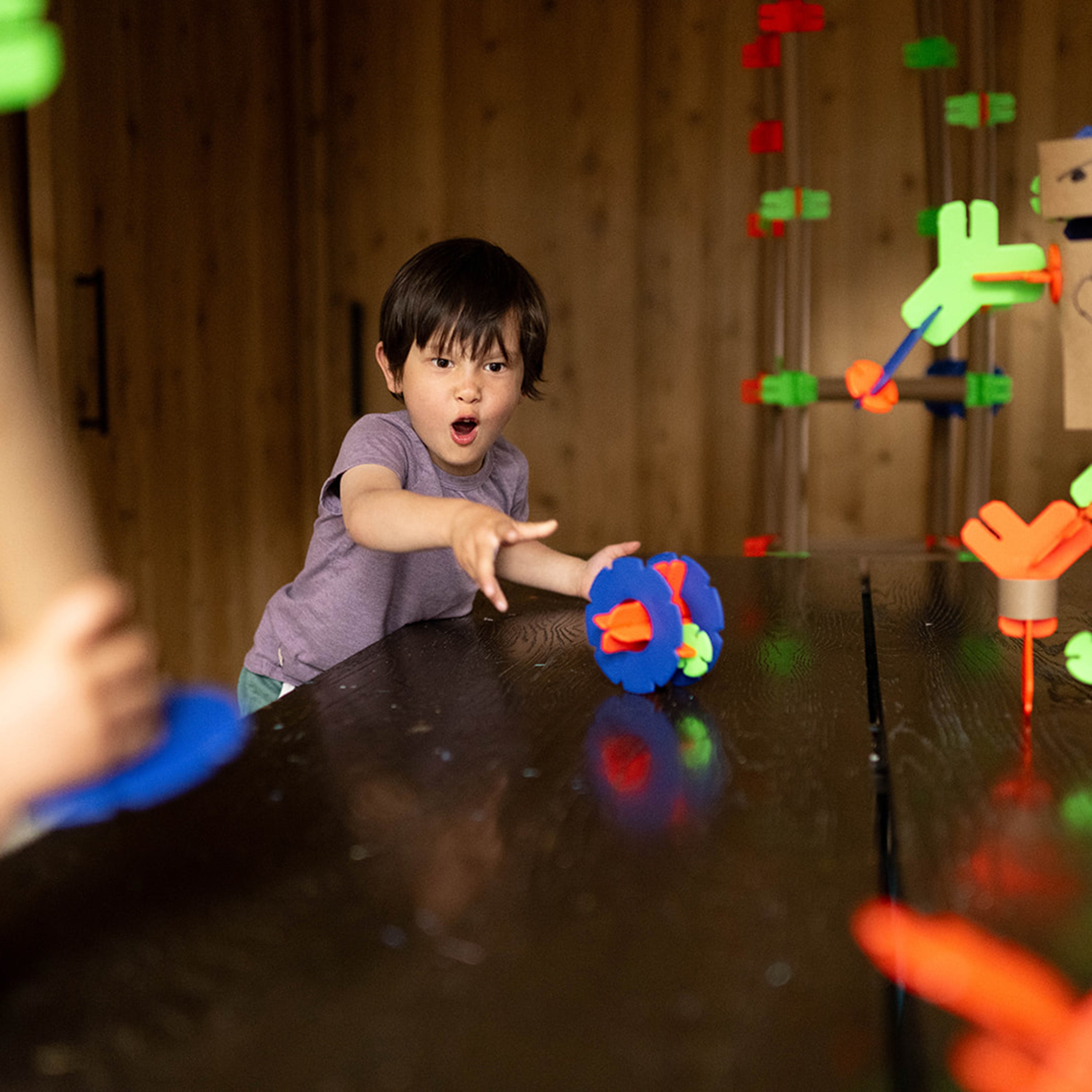 Child playing with colorful toys at a table in a room with wooden walls.
